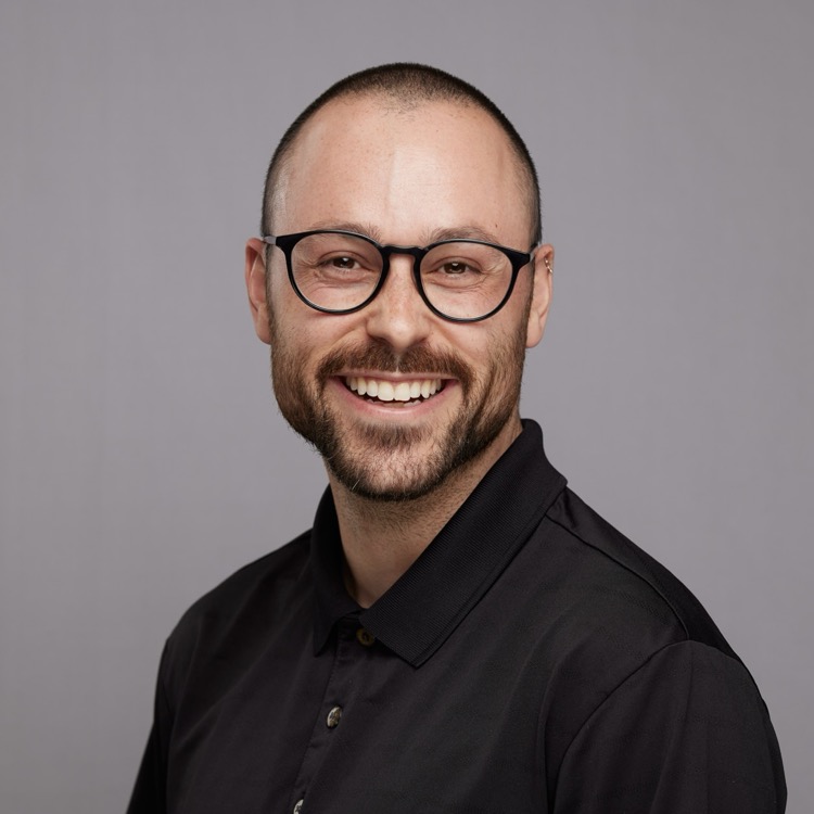 Jack Rome, smiling, wearing glasses and a black collared shirt.